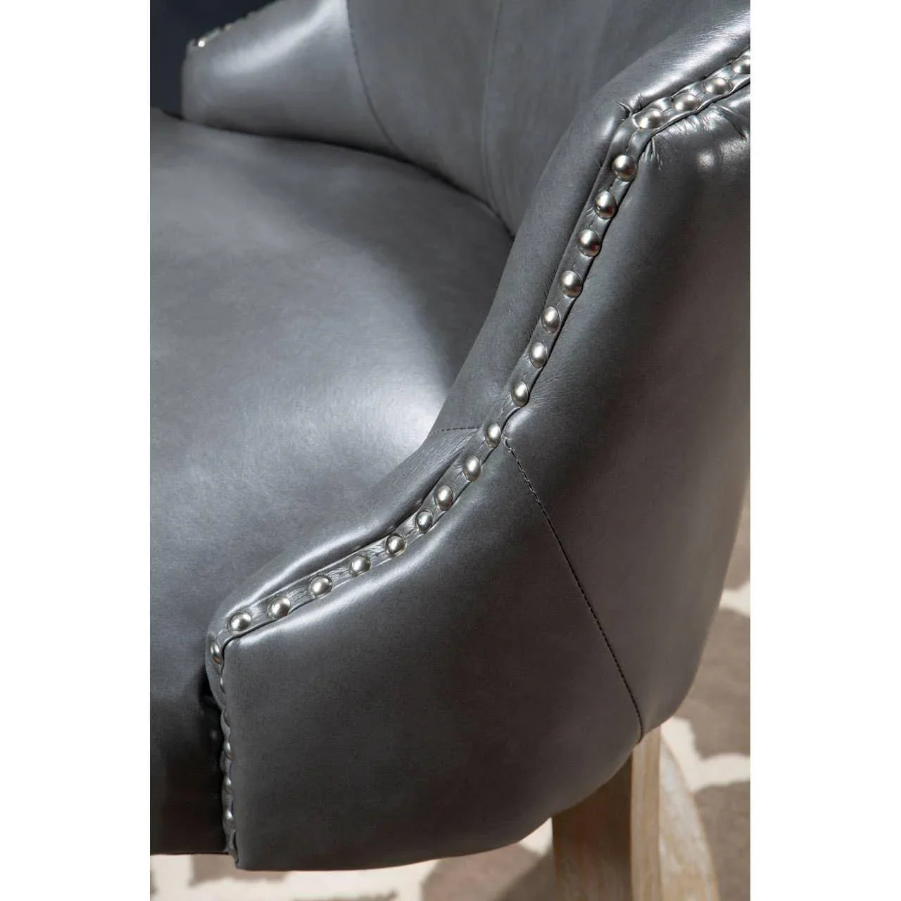 Grey leather accent chair with silver stud detailing and light wood legs close-up