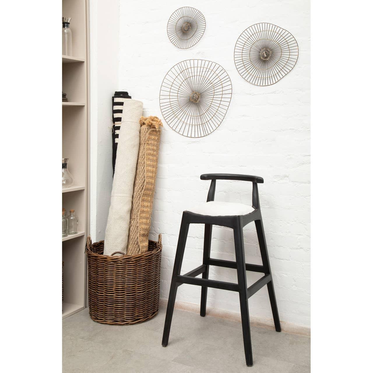 Black wooden bar stool with white seat beside wicker basket and rolled rugs in modern room