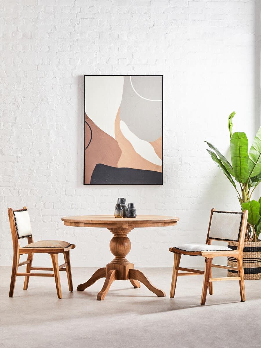 Round wooden dining table set with two cushioned chairs in modern room