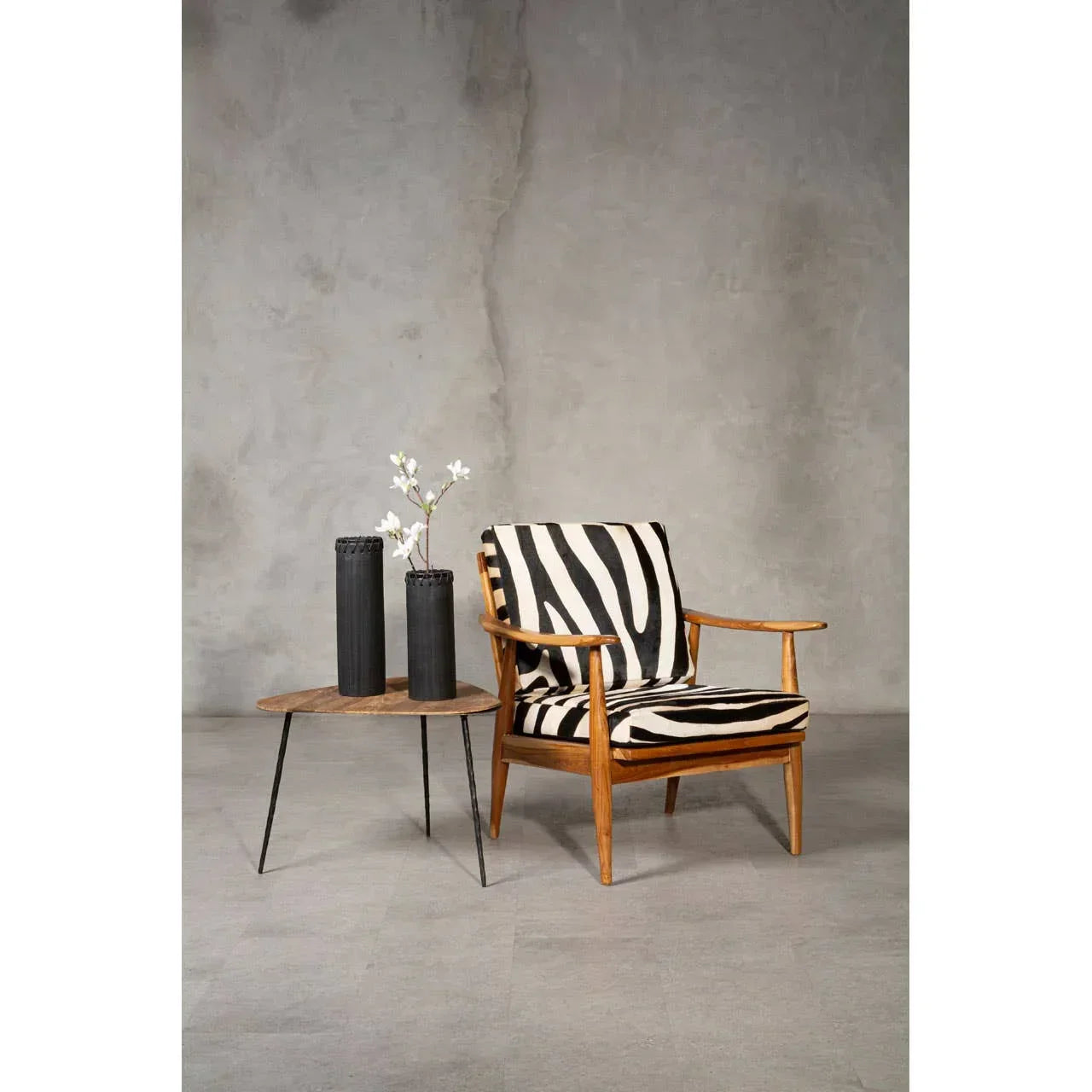 Zebra print armchair with wood frame beside round wooden side table and black vases