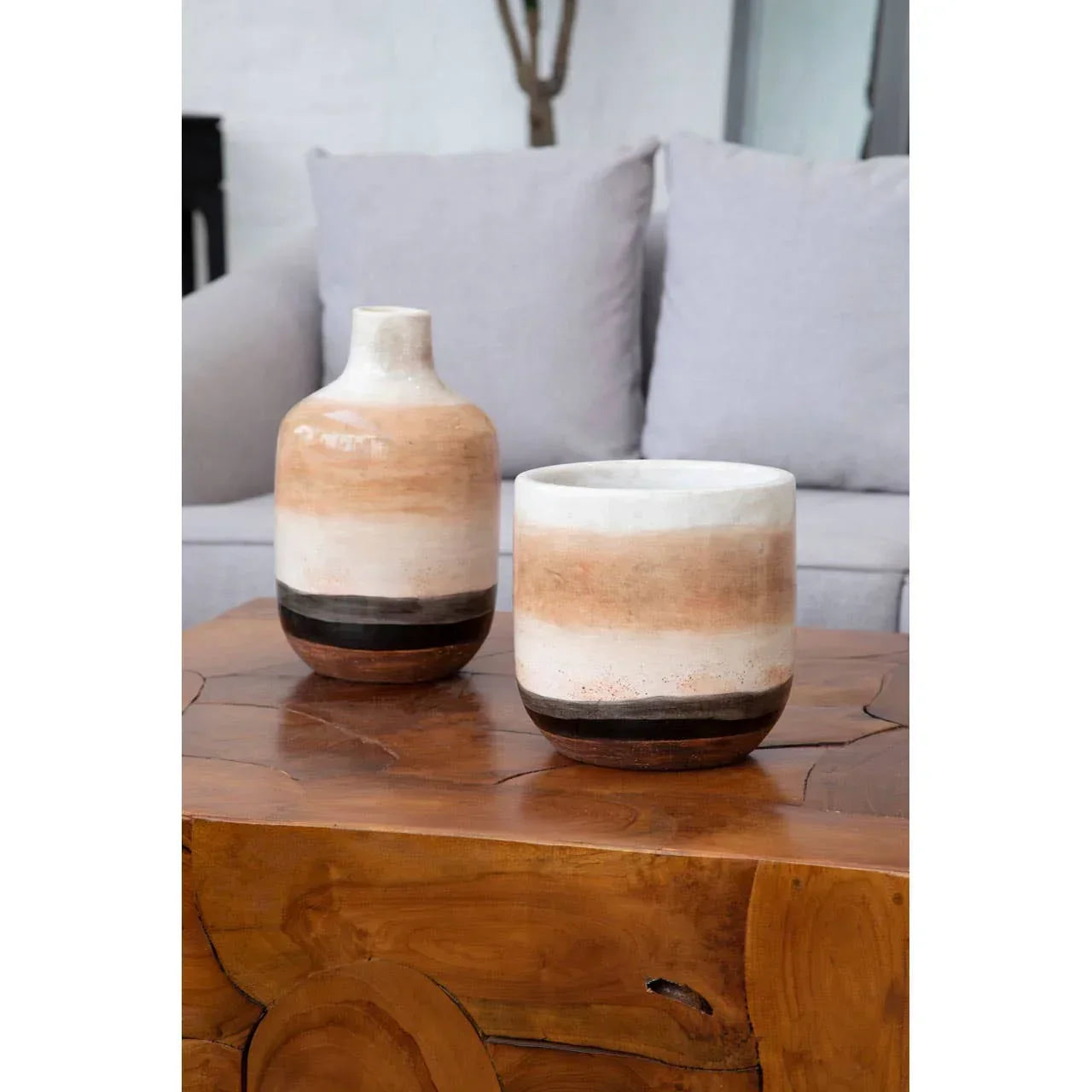 Ceramic vase and planter in neutral tones on wooden coffee table, grey sofa in background