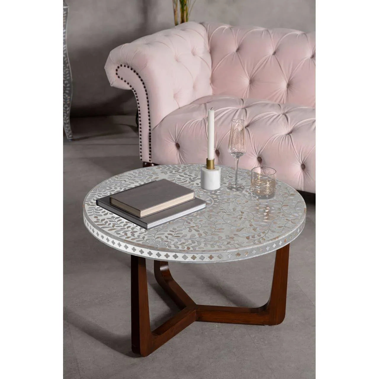 Round bone inlay coffee table with wooden legs set by a pink tufted sofa