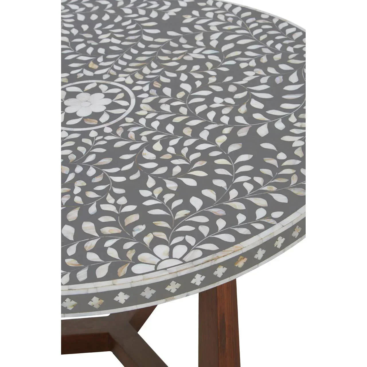 Round dining table with grey surface and white floral inlay pattern, wood legs visible