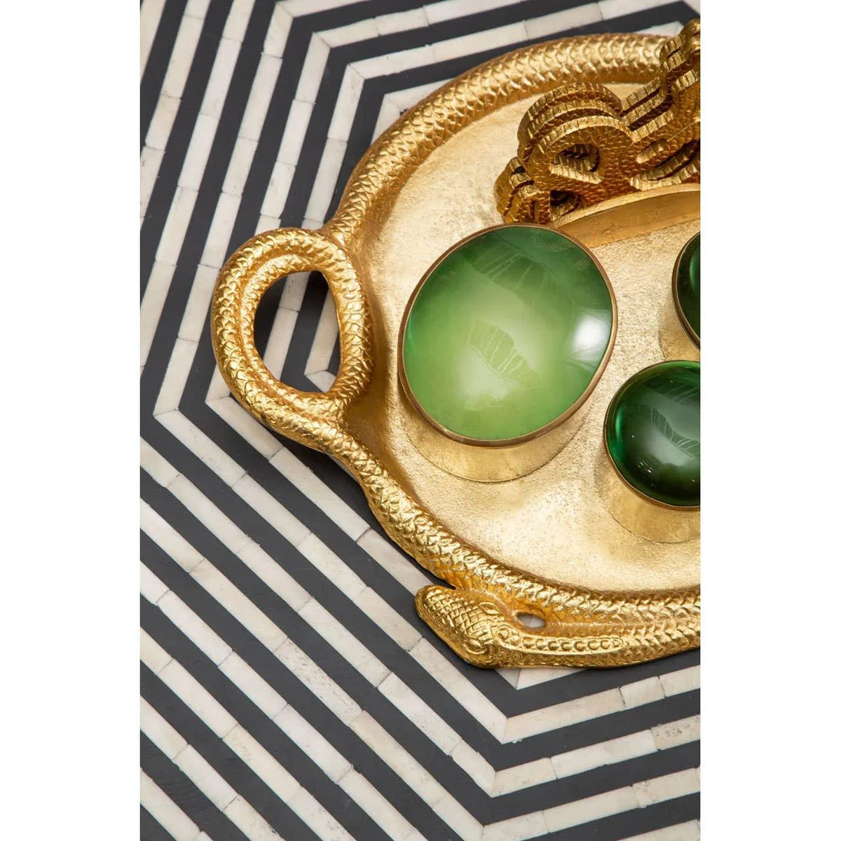 gold decorative tray with snake handles and green stone accents on geometric table