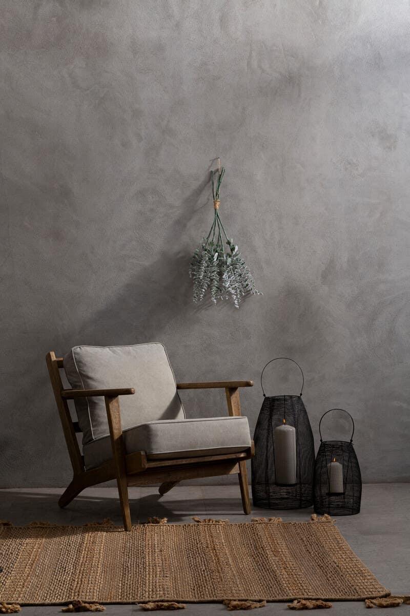 Wooden armchair with grey cushions beside woven candle holders and jute rug in minimal room