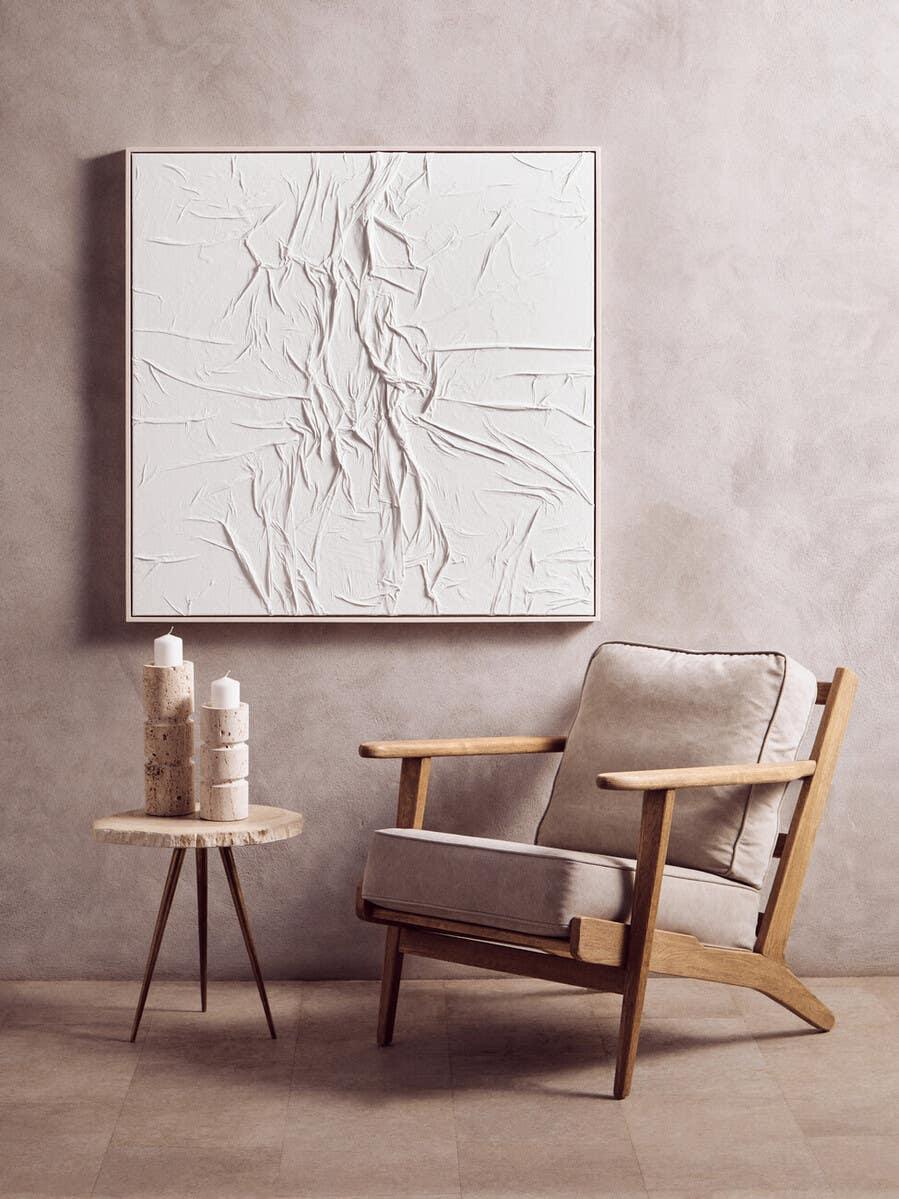 Modern wooden armchair with beige cushions beside round side table and candles in neutral room