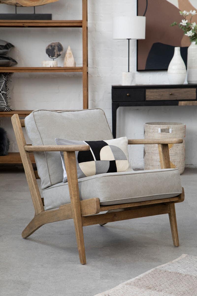 Light grey armchair with wooden frame and patterned cushion in modern living room setting