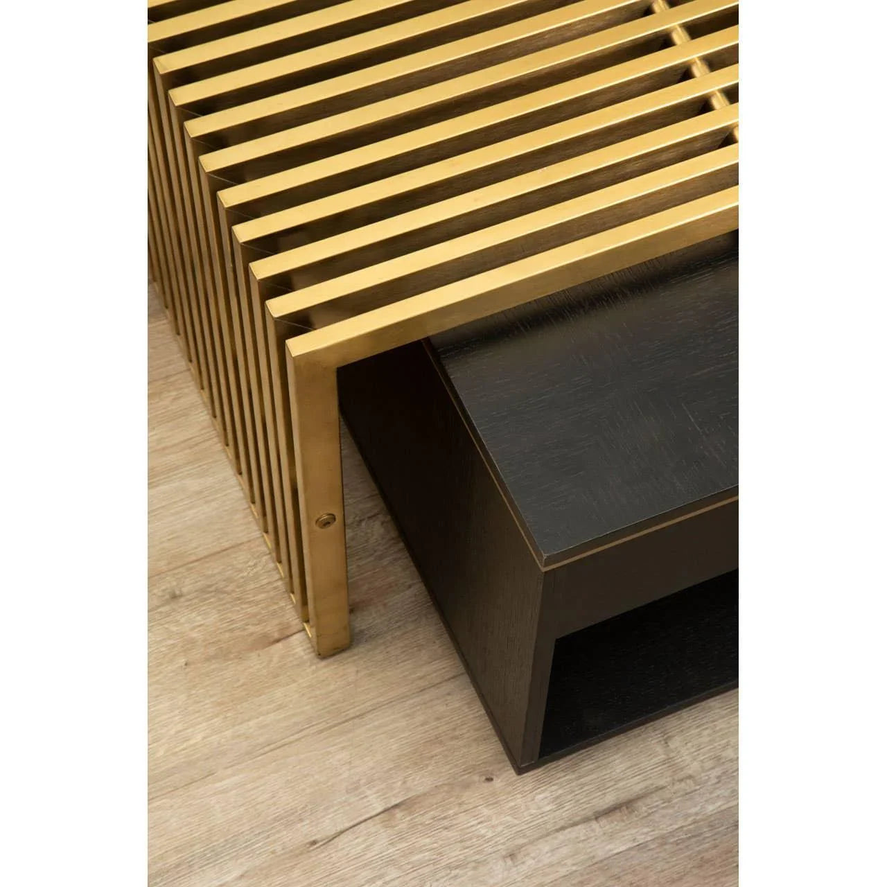 Modern coffee table with gold metal slats and black wooden shelf on light wood floor