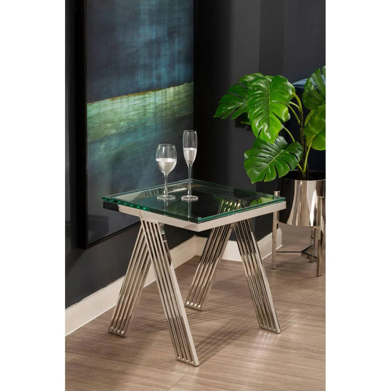 Glass top side table with chrome legs, two wine glasses, and modern decor setting