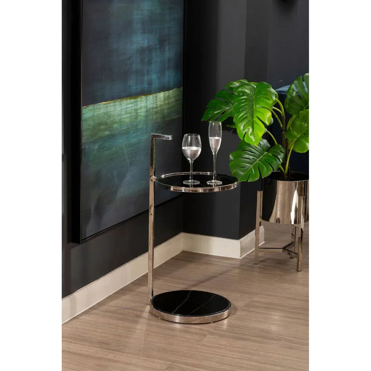 Round black marble side table with chrome frame holding two glasses in a modern living room