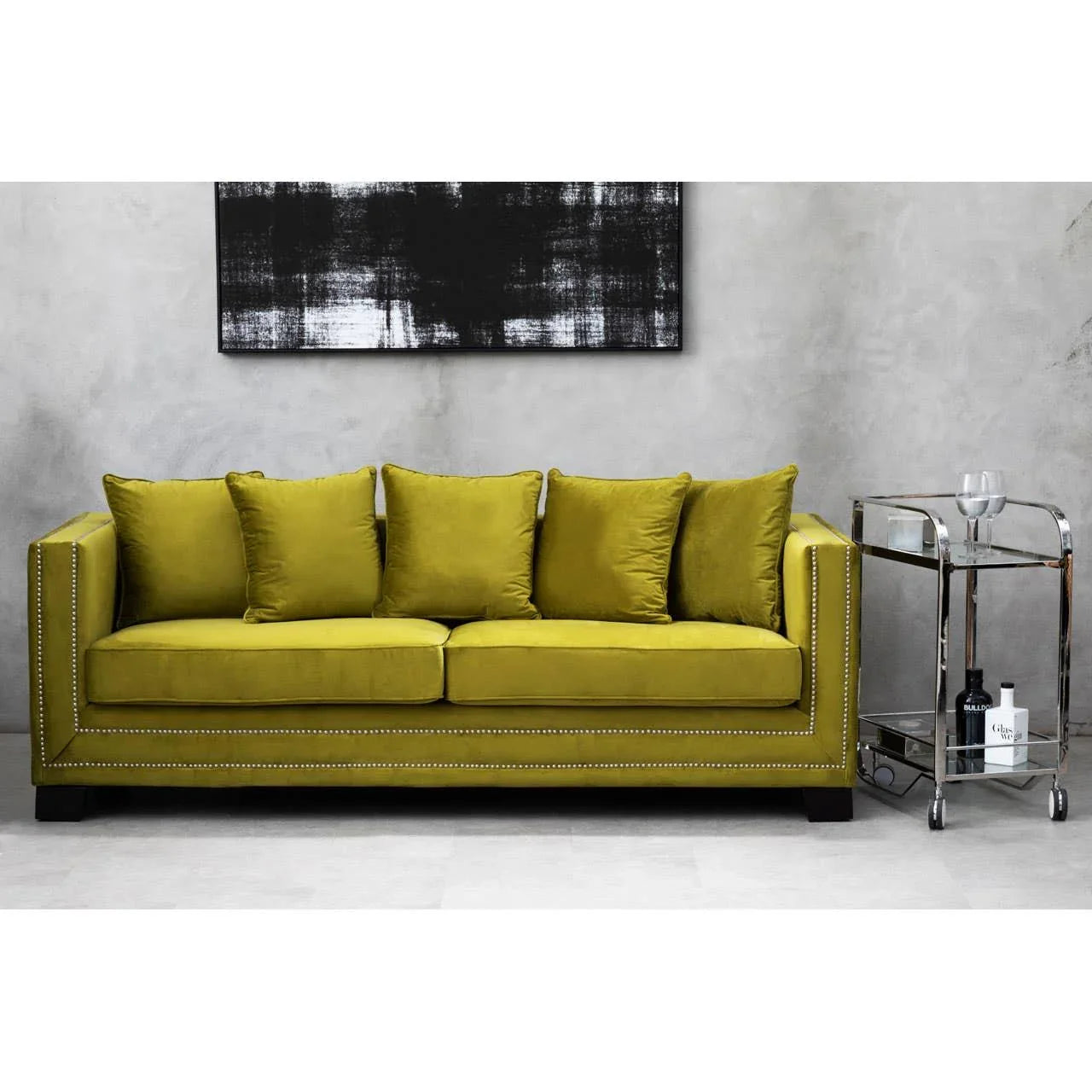 Olive green velvet sofa with stud detailing, matching cushions, and metal drinks trolley beside it