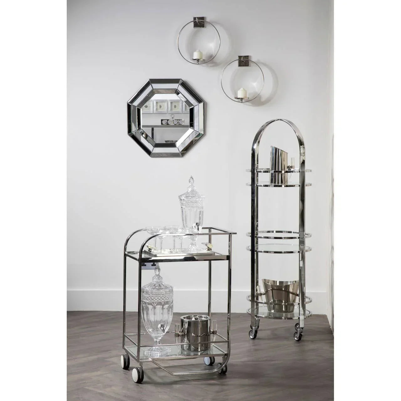 Chrome drinks trolley with glass shelves and glassware beside chrome wine rack in modern room