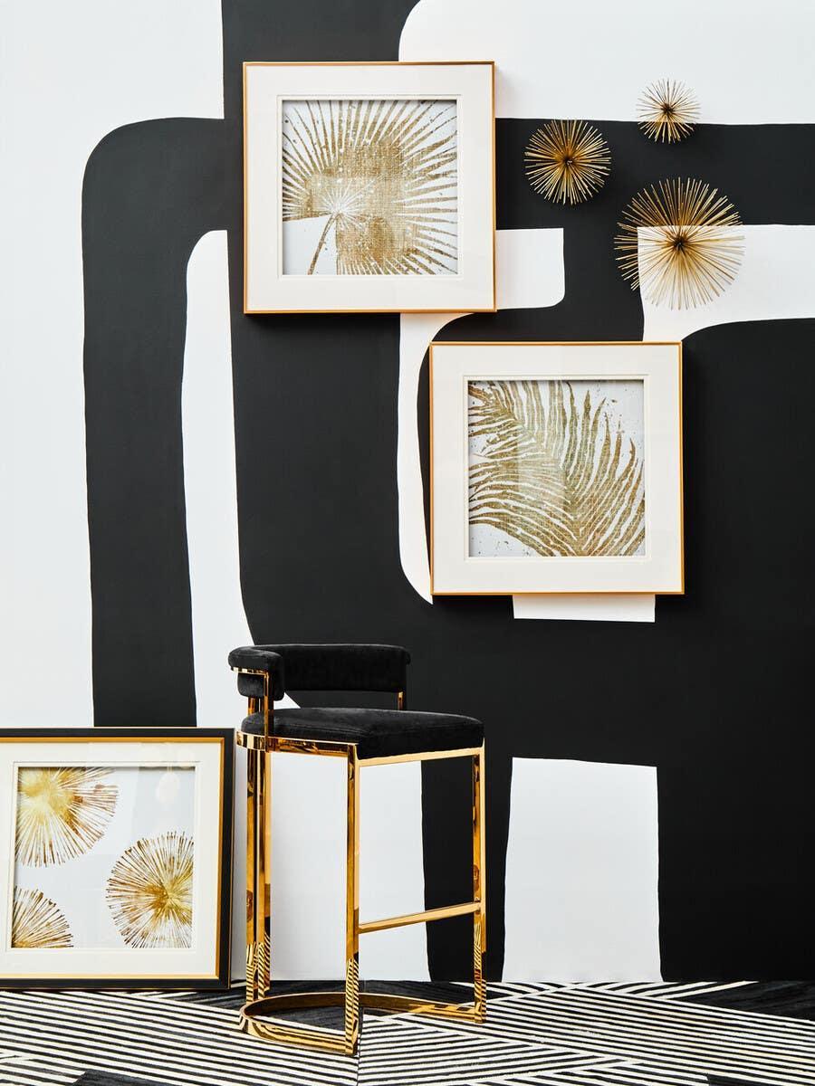 Modern gold and black bar stool against abstract wall art and framed botanical prints