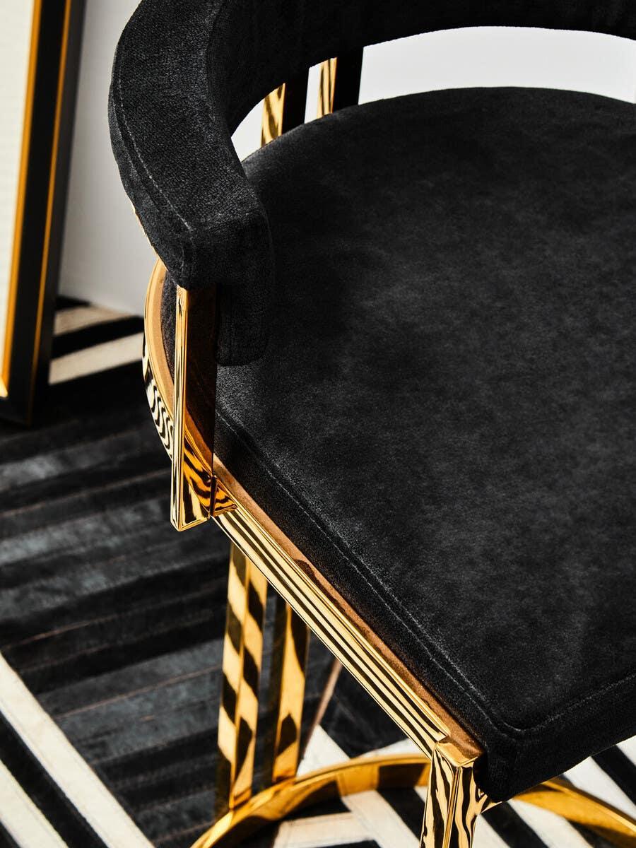 Black velvet dining chair with gold metal frame and curved backrest on striped rug
