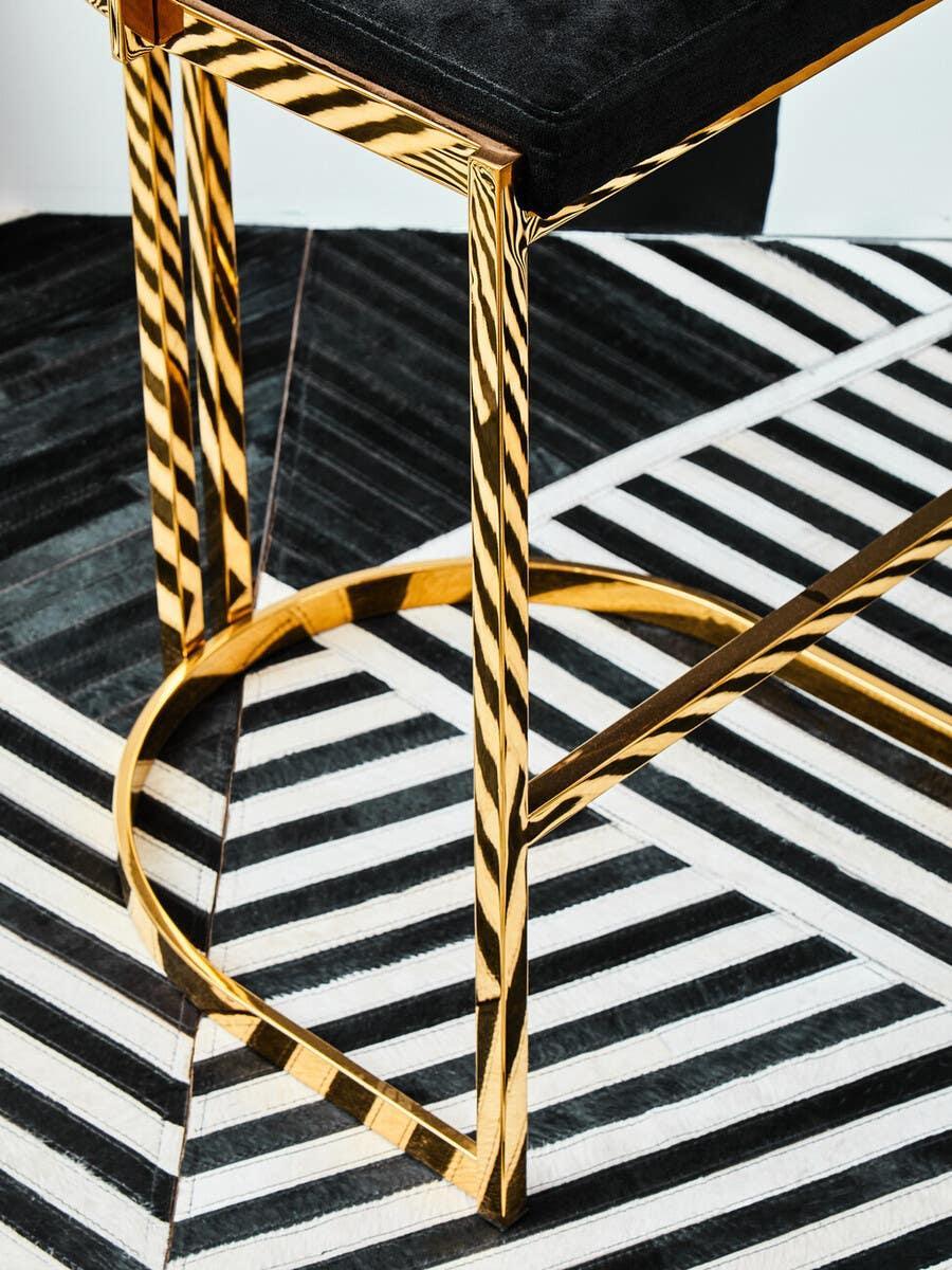Gold metal bar stool base with black upholstered seat on geometric patterned floor