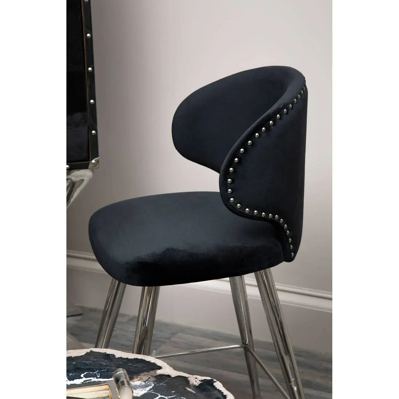 Black velvet dining chair with silver stud trim and chrome legs beside marble table