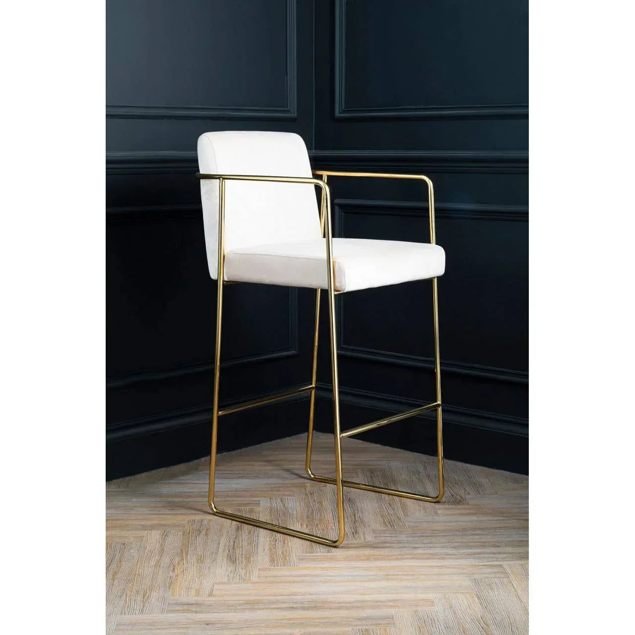 White bar stool with gold metal frame and arms on herringbone wood floor