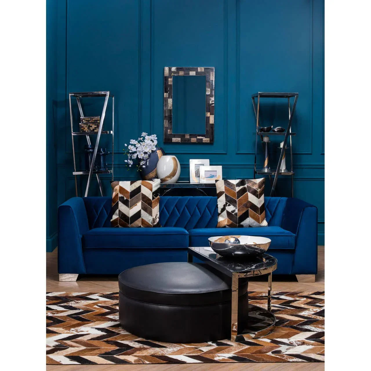 Blue velvet sofa with patterned cushions, black ottoman, and modern shelving in living room