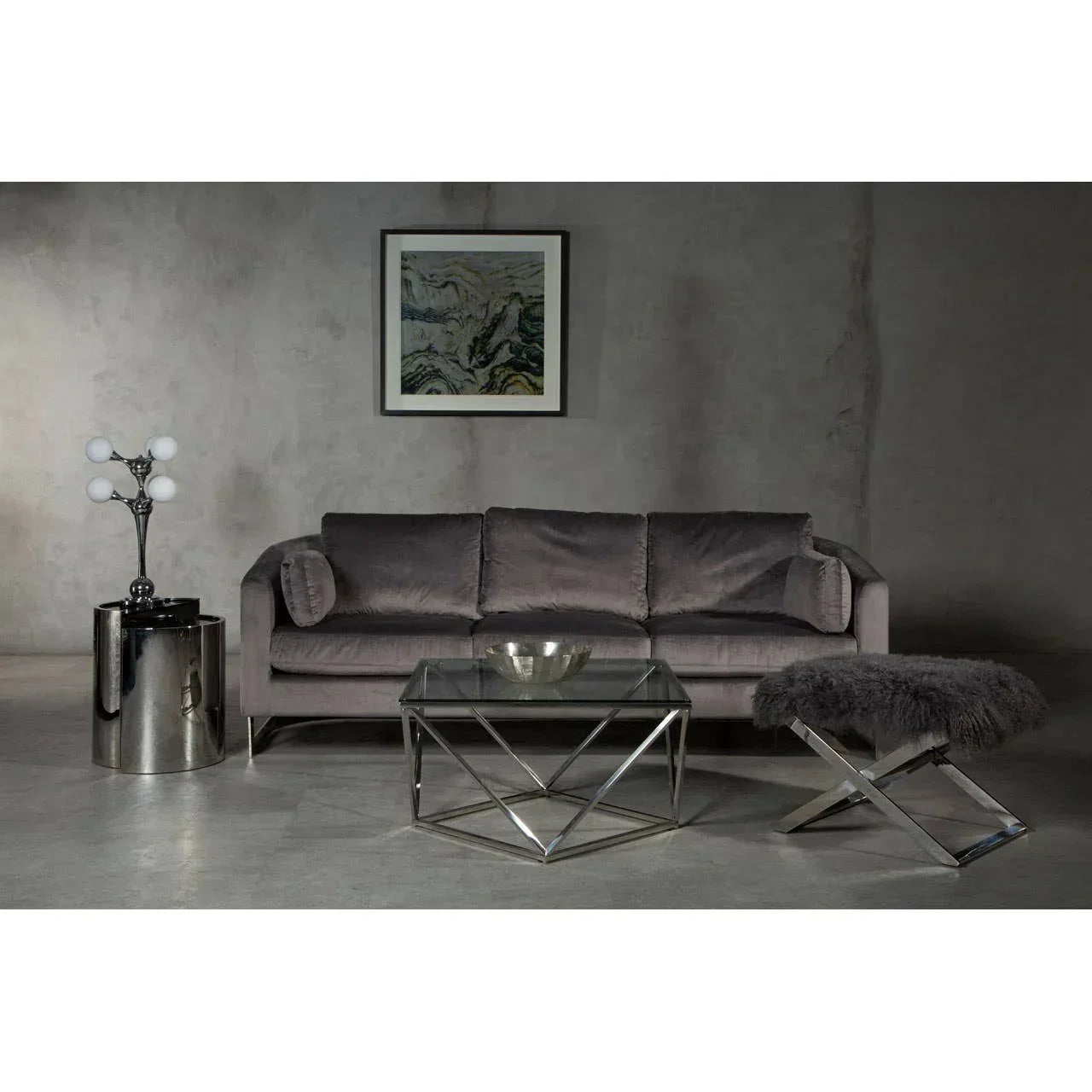 Grey velvet sofa with glass coffee table and chrome side table in modern living room setting