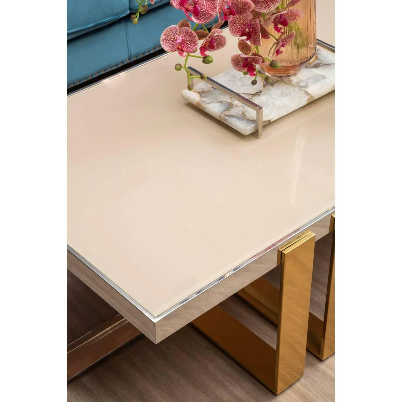 Glossy beige coffee table with gold metal legs, marble tray, and pink flowers, close view