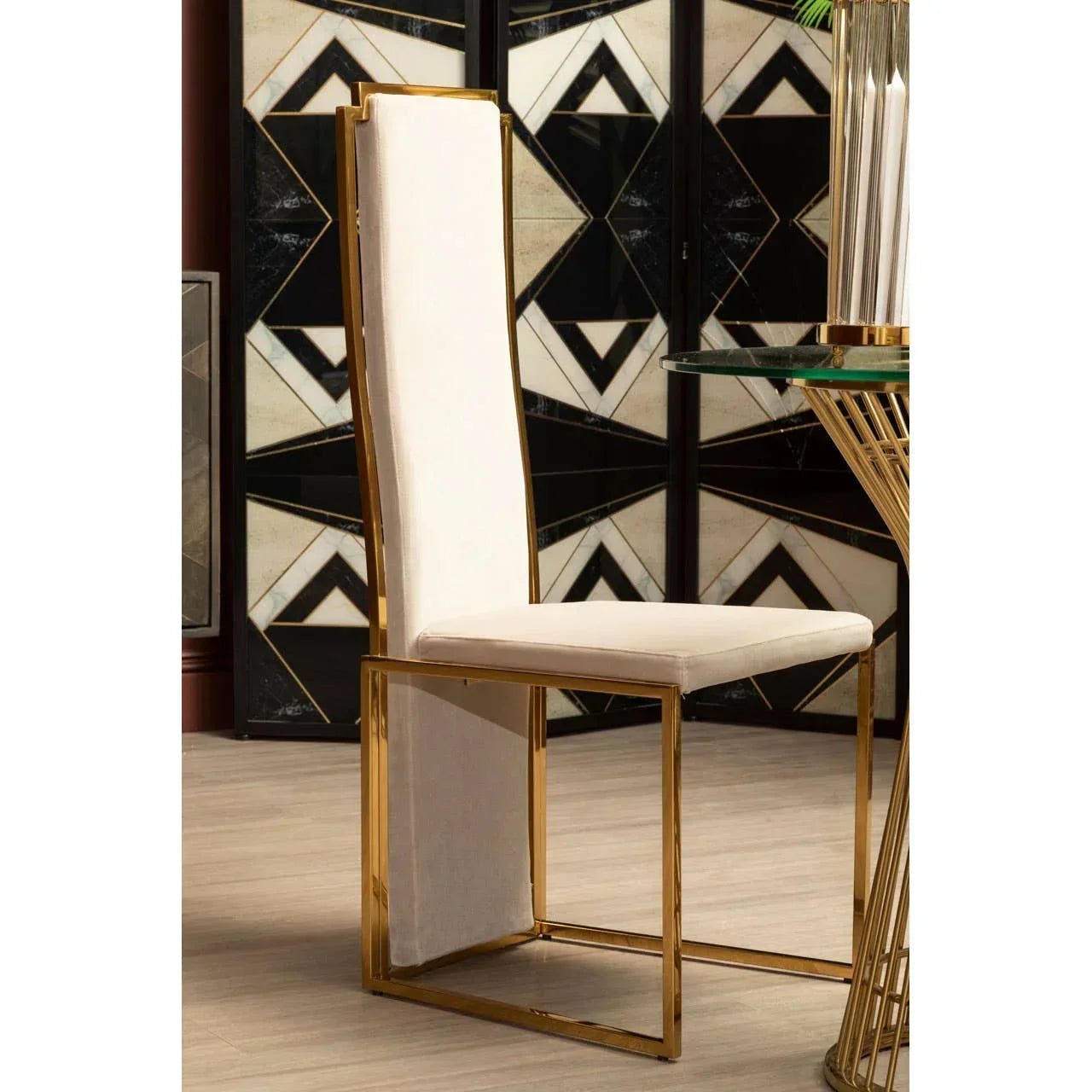 Modern dining chair with gold metal frame and cream upholstered seat beside glass table