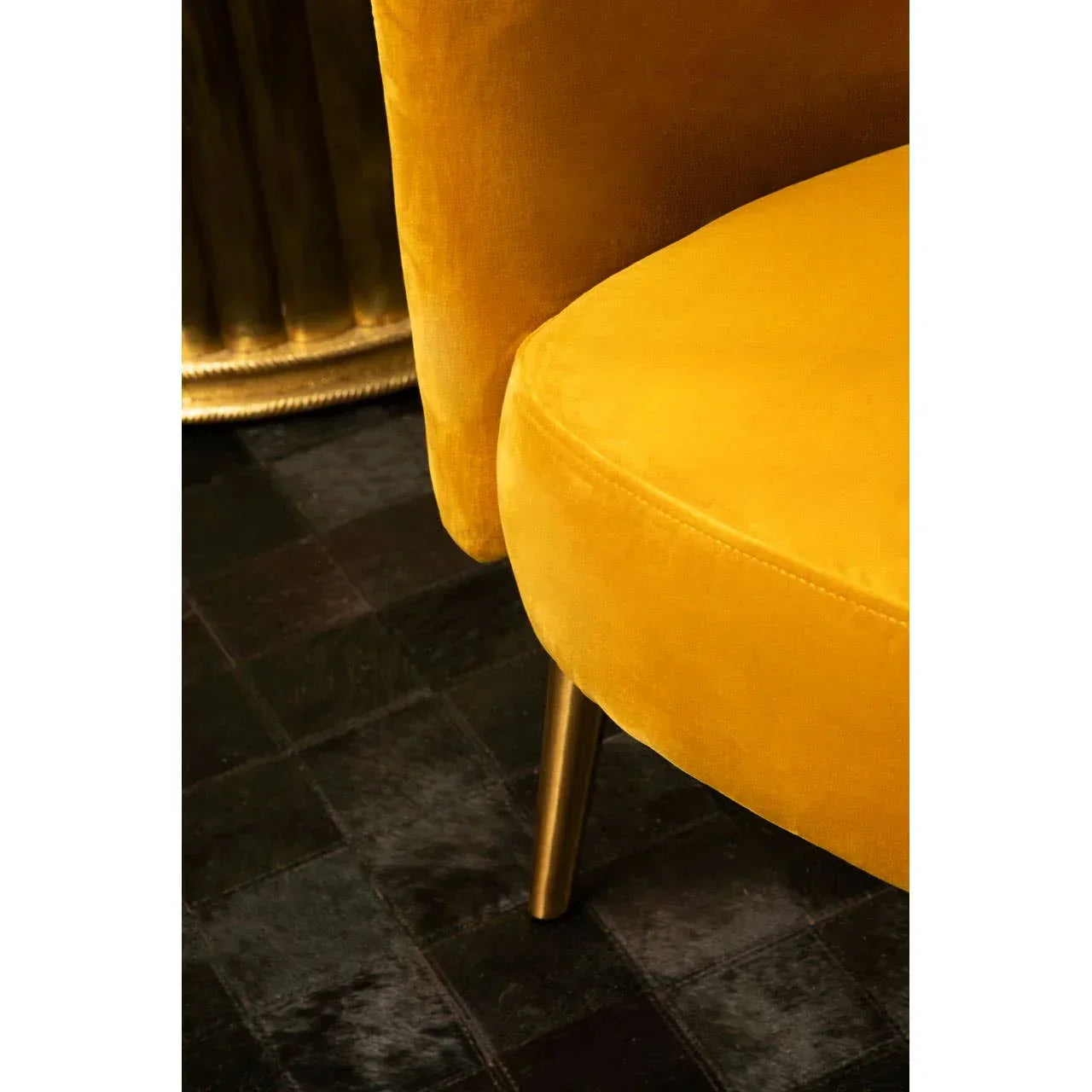 Mustard velvet accent chair with gold metal leg on dark tiled floor