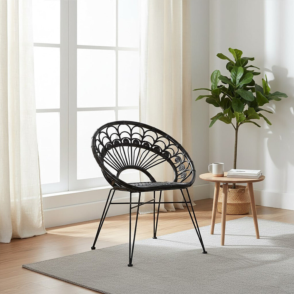 A black natural rattan chair with a circular backrest and slender legs, positioned in a bright room with large windows. A small round wooden side table is next to the chair, and a potted plant adds a touch of greenery to the space. Light-colored curtains frame the windows, enhancing the airy atmosphere