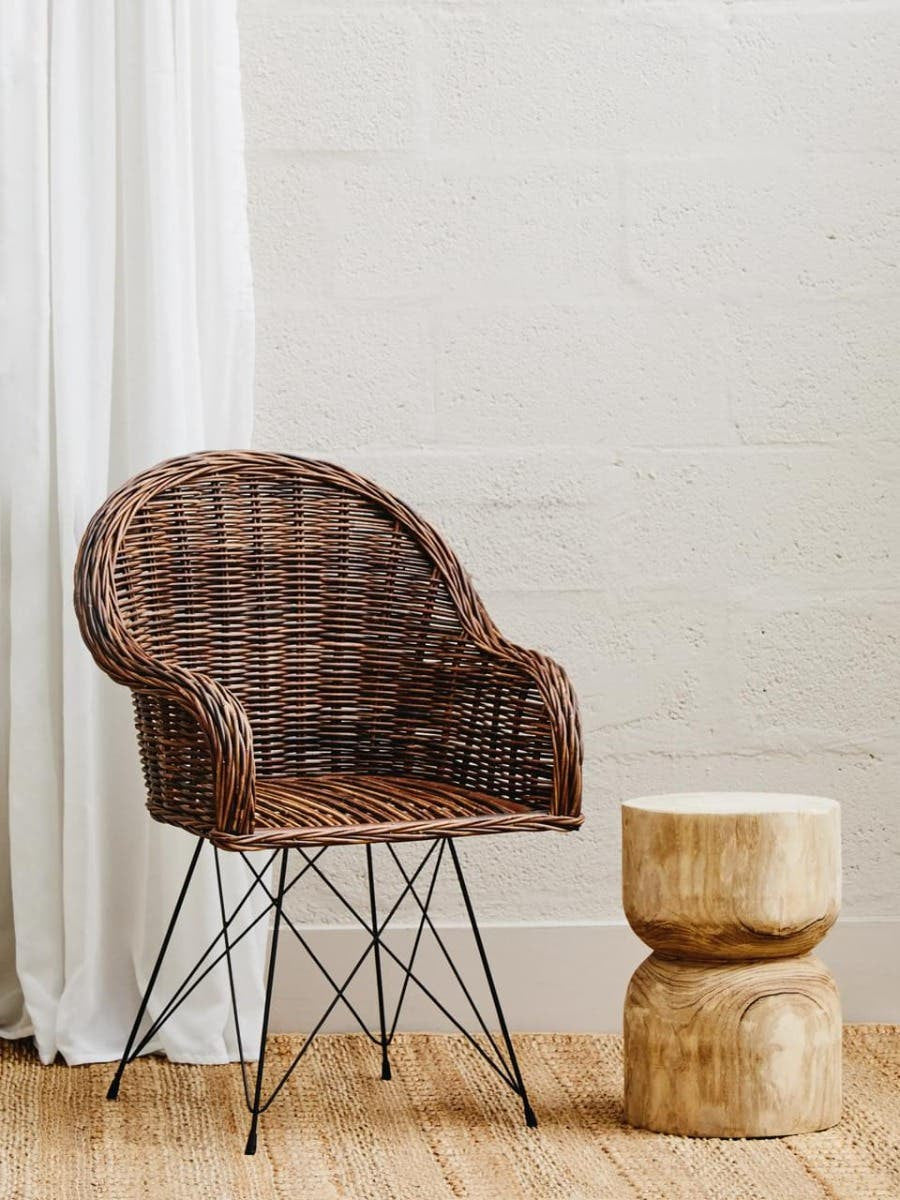Natural croco rattan chair with a curved backrest and metal legs, positioned next to a round wooden side table, set against a light-colored wall and wooden floor