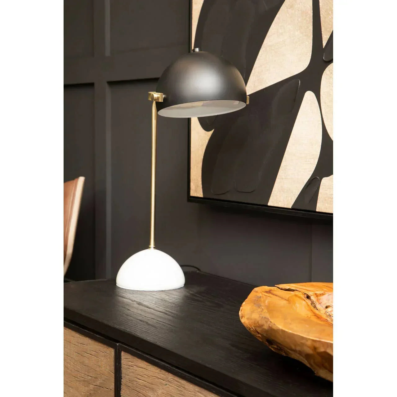 Modern black and brass table lamp with white base on sideboard against abstract wall art