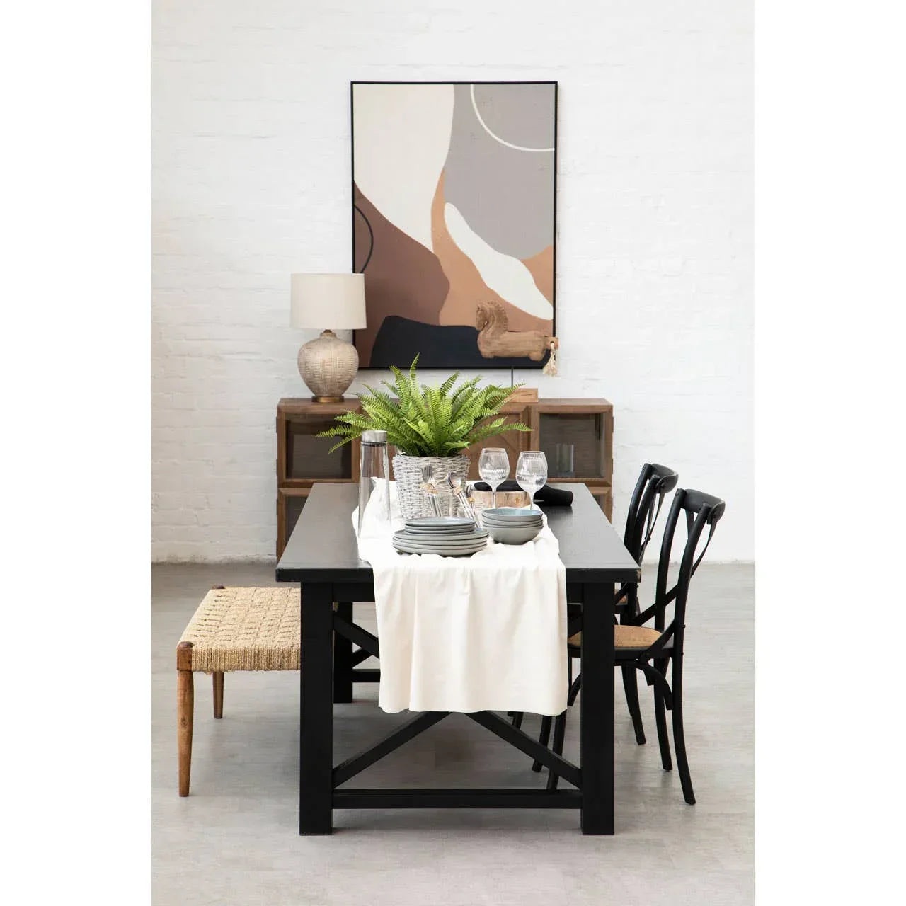 Black wooden dining table set with ceramic plates, glasses, and a woven bench