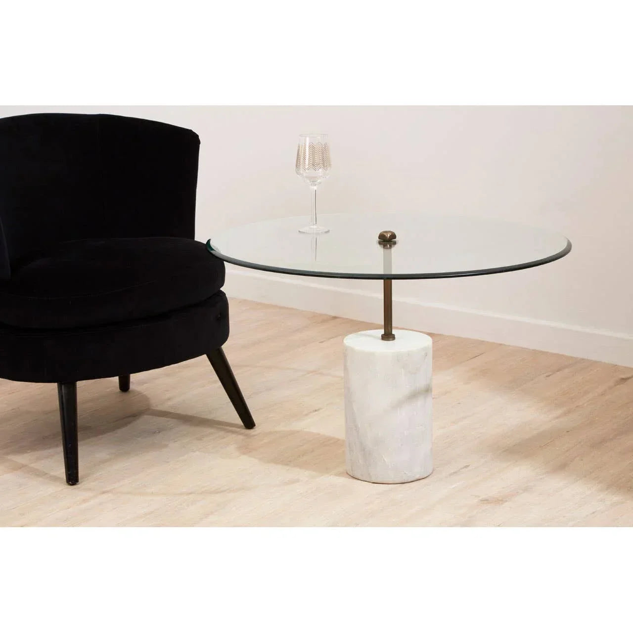Round glass coffee table with marble base beside black velvet chair on wooden floor
