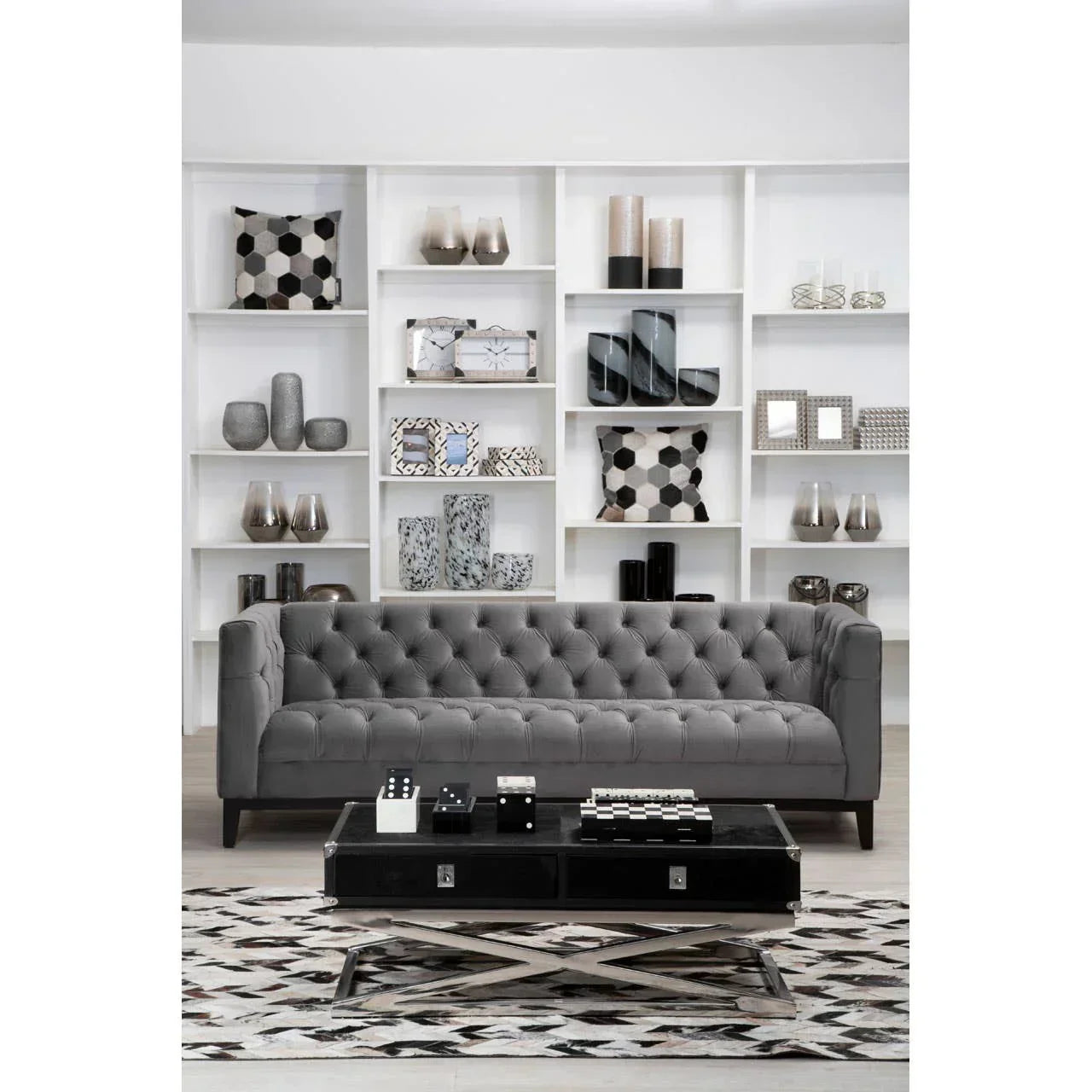 Grey tufted velvet sofa in modern living room with patterned cushions and decorative shelving