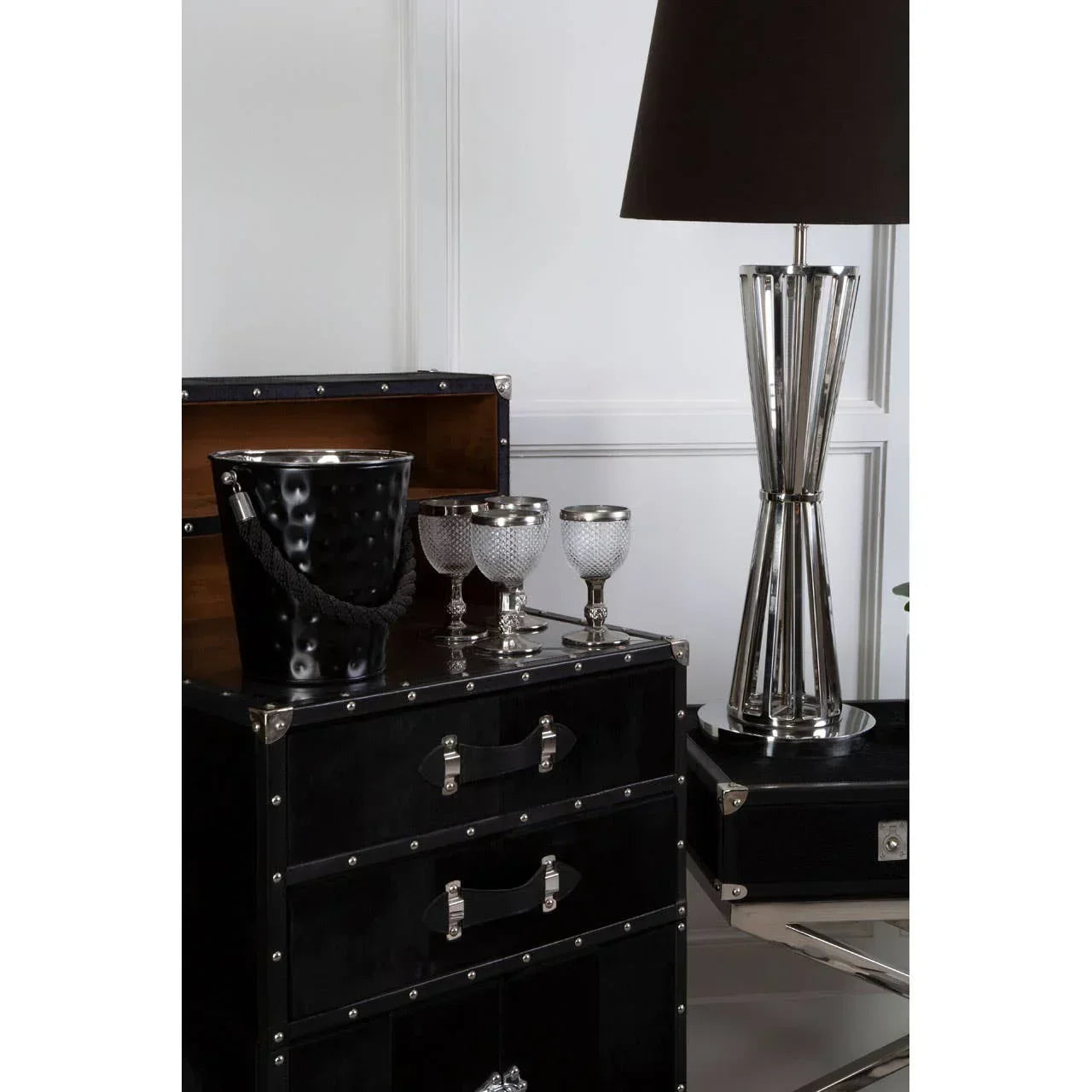 Black trunk cabinet with silver lamp, ice bucket, and three decorative wine glasses on top