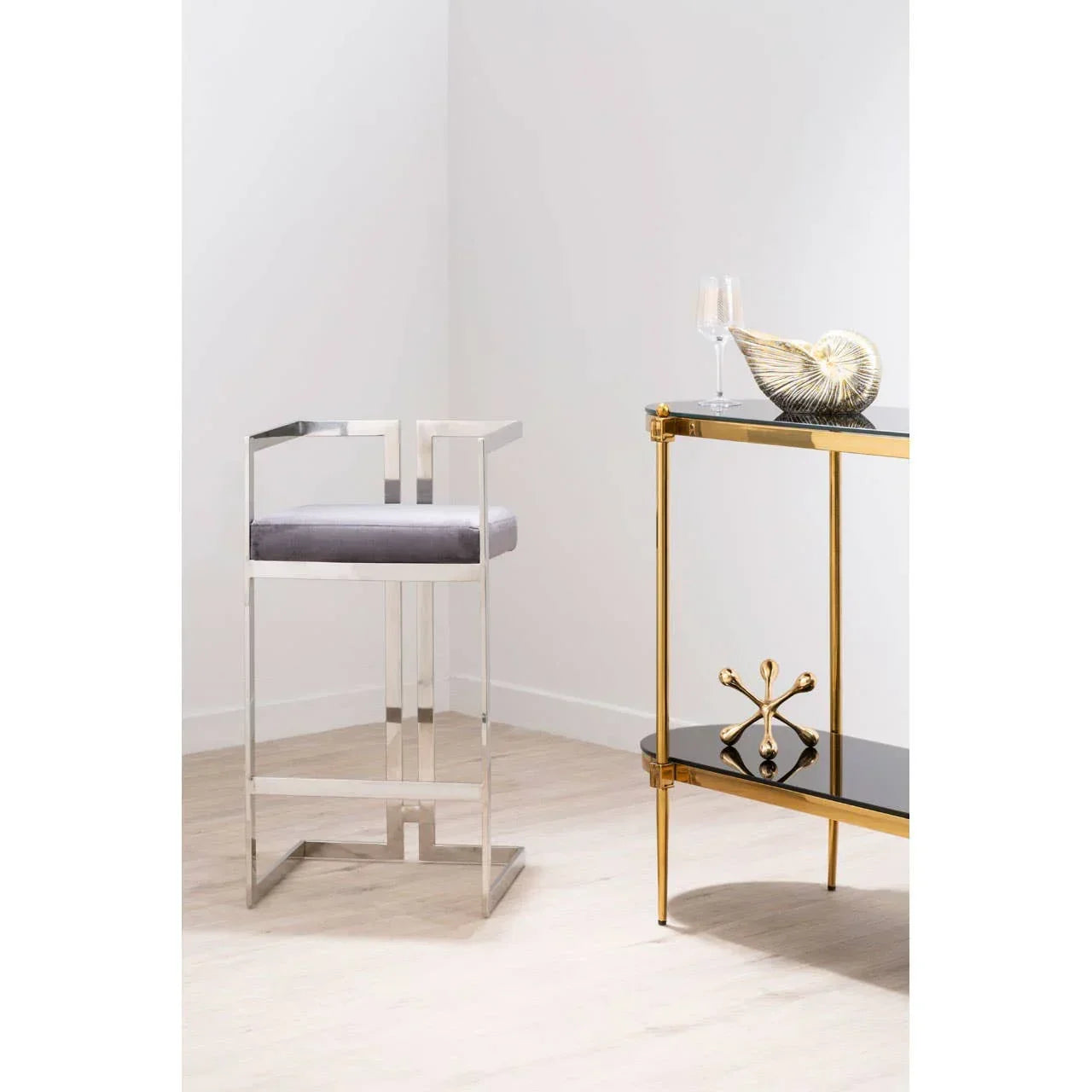Modern bar stool with silver metal frame and grey seat beside gold and black console table