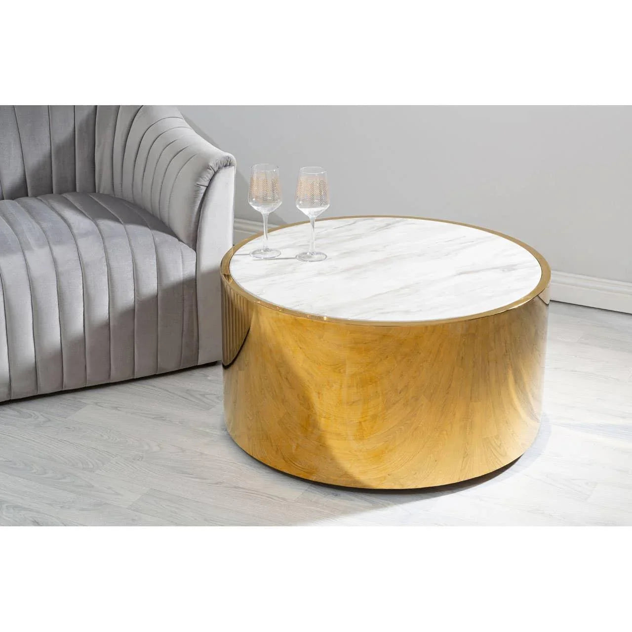 Round marble coffee table with gold metal base beside grey velvet sofa on light wood floor