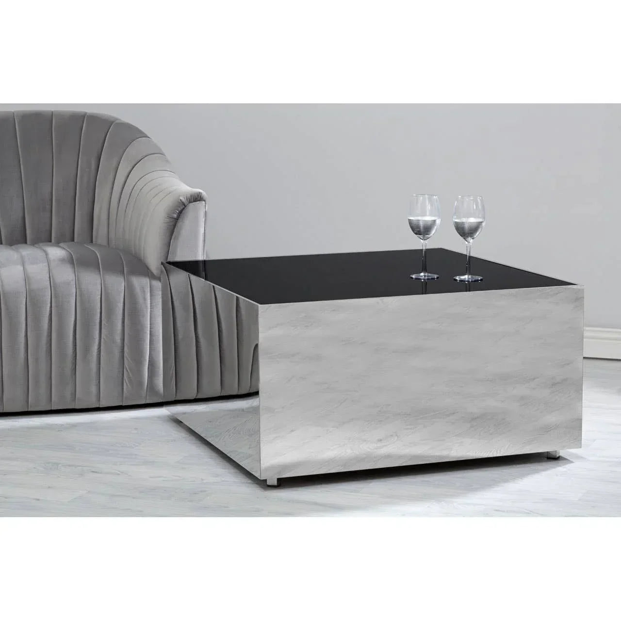 Modern square coffee table with black glass top beside grey velvet sofa in living room setting