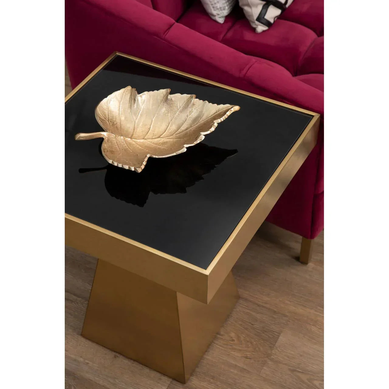 Gold and black square side table with metallic leaf bowl beside red velvet sofa