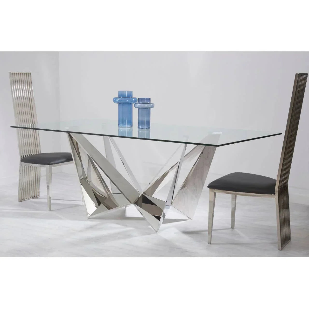 Glass dining table with geometric chrome base and two high-back metallic chairs