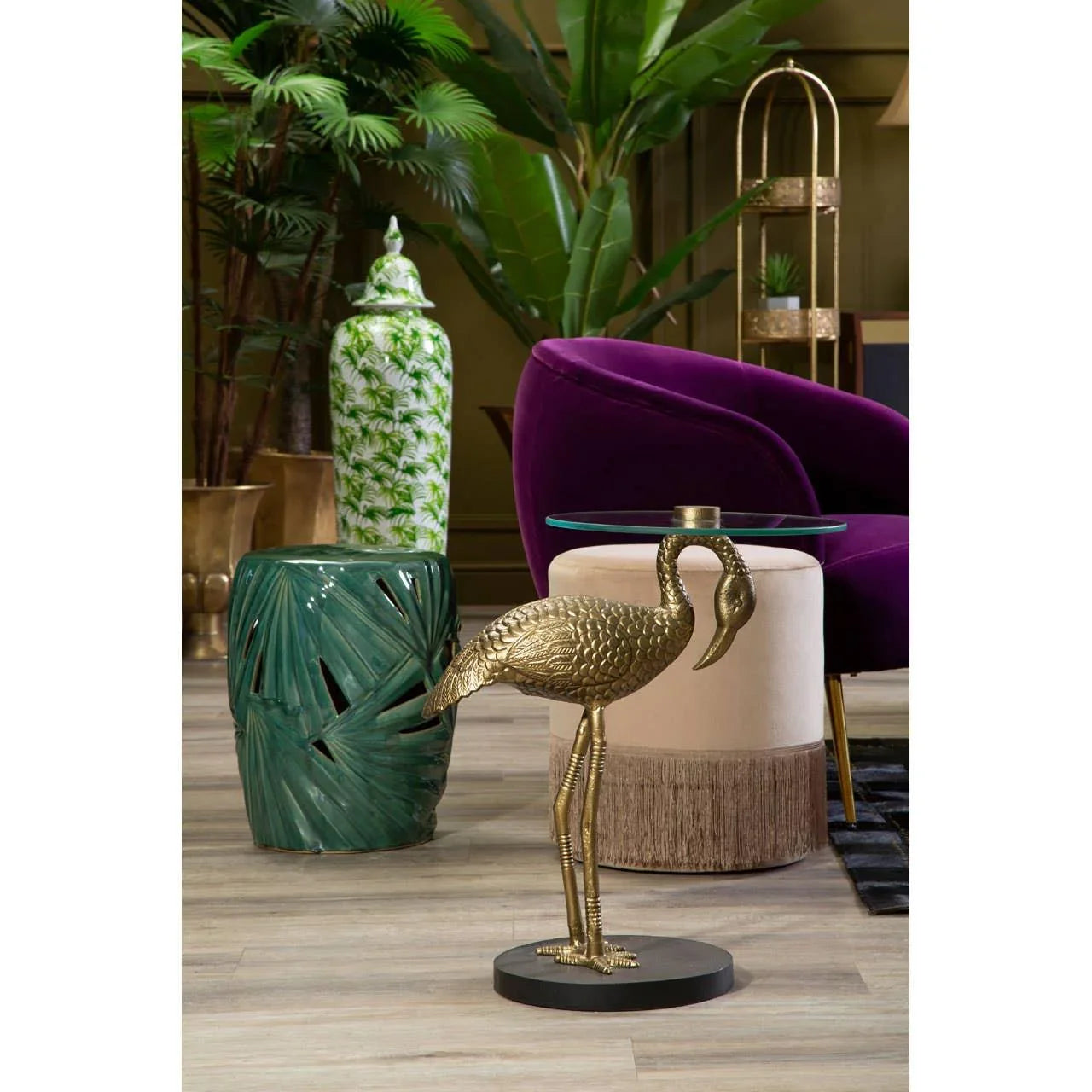 Gold bird side table with glass top beside green ceramic stool and purple velvet accent chair