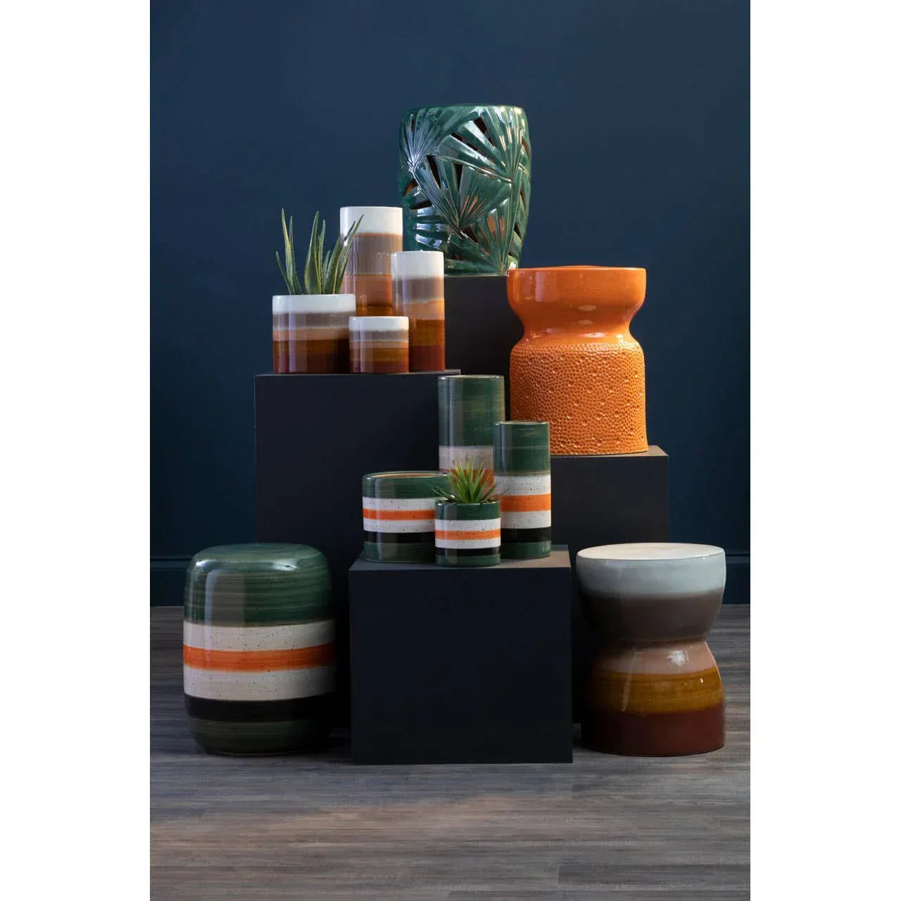 Ceramic vases and stools in green, orange, and brown tones on display stands