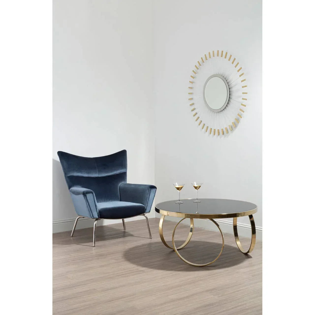 Blue velvet accent chair beside gold and glass coffee table with art deco wall mirror