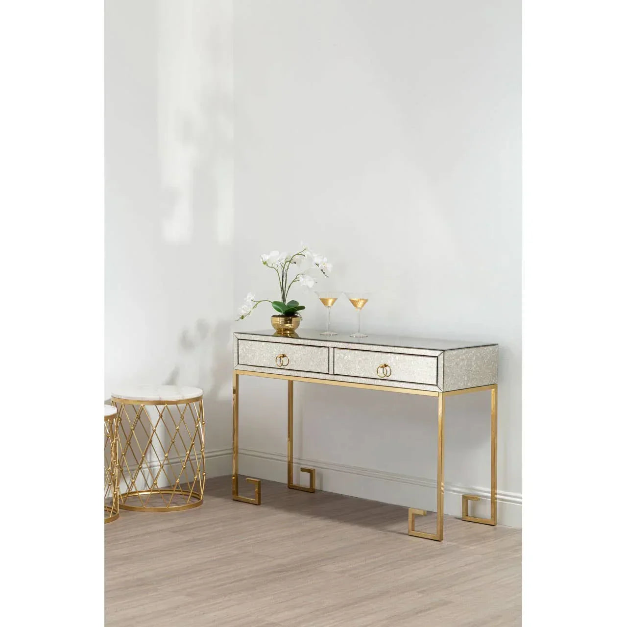 Mirrored console table with gold frame, two drawers, orchid plant, and drinks in modern room