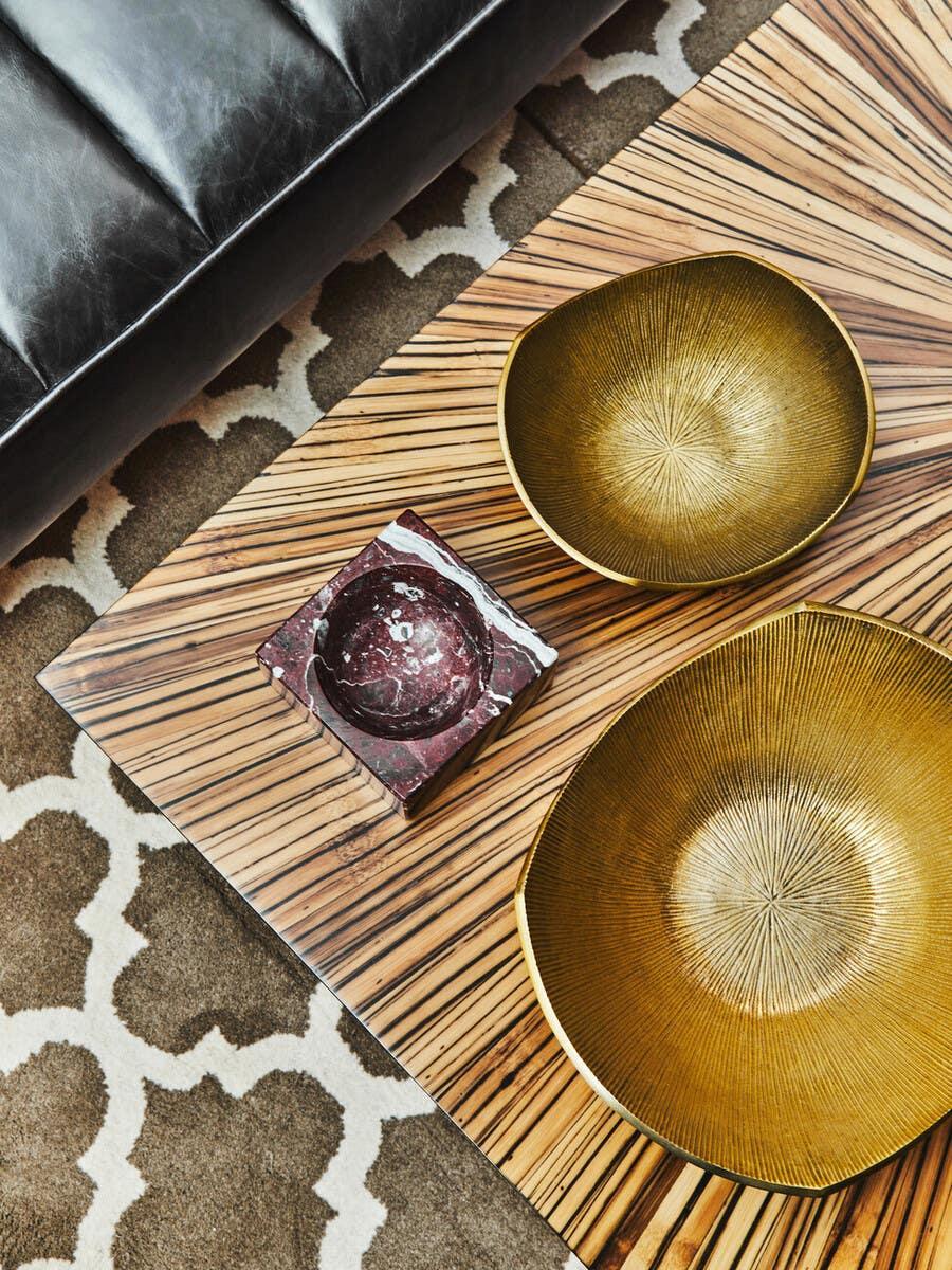 Striped wood coffee table with gold decorative bowls and marble dish beside leather sofa