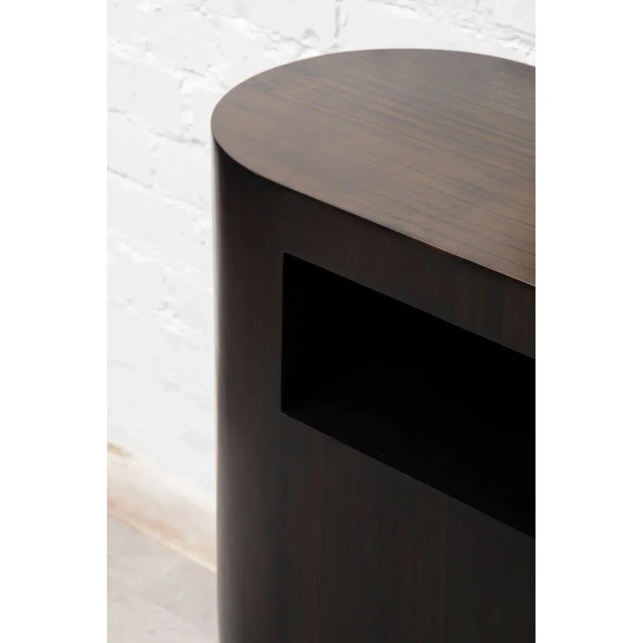 Dark wood side table with rounded edge and open storage shelf against white wall