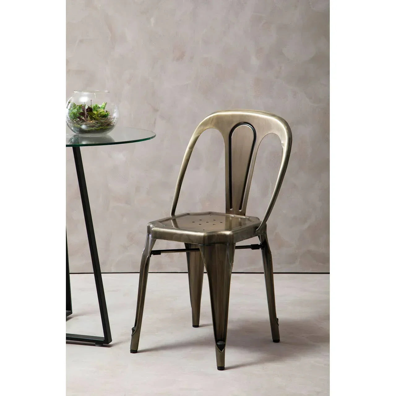 Metal dining chair with curved back beside glass table on neutral-toned floor