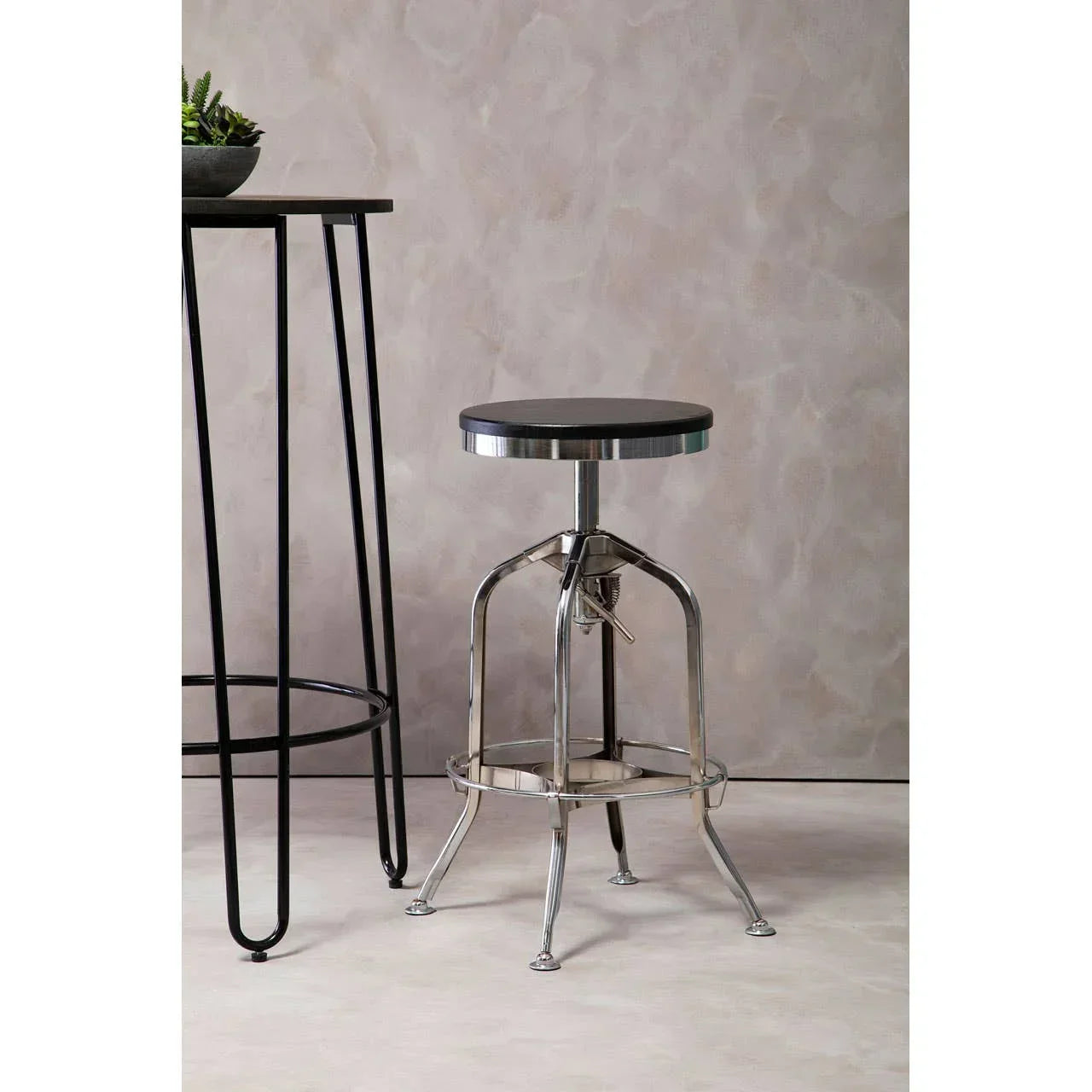 Industrial bar stool with metal legs and black seat next to a tall black dining table