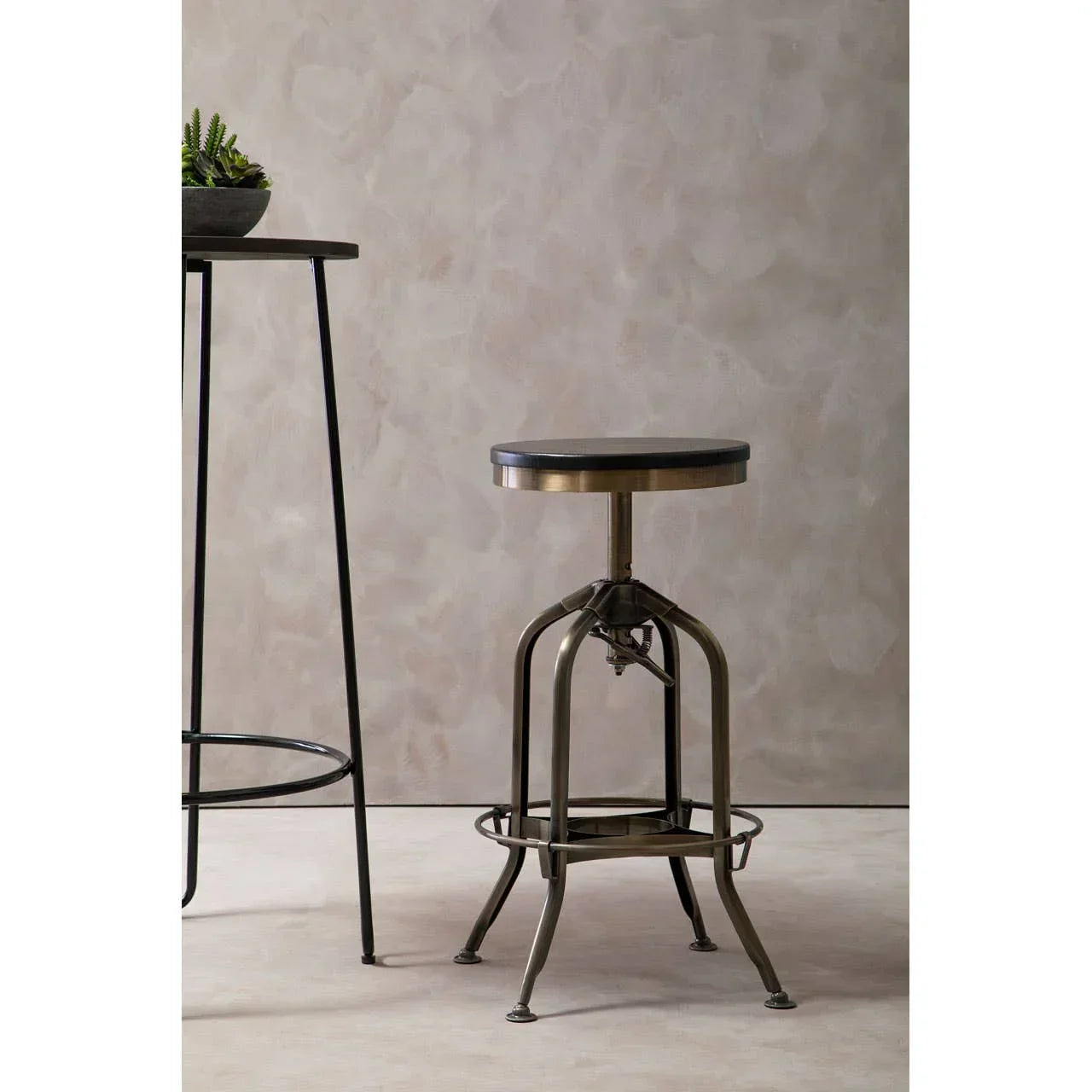 Industrial metal bar stool with round wooden seat beside tall black bar table