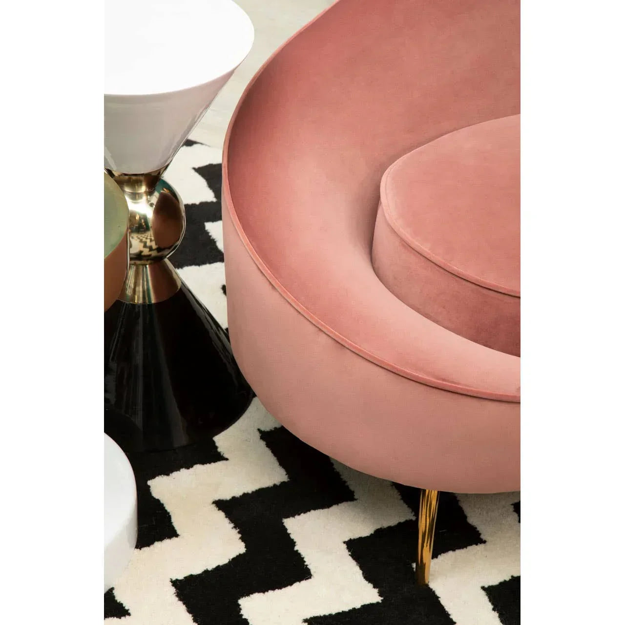 Curved pink velvet sofa with gold legs beside modern side table on chevron rug