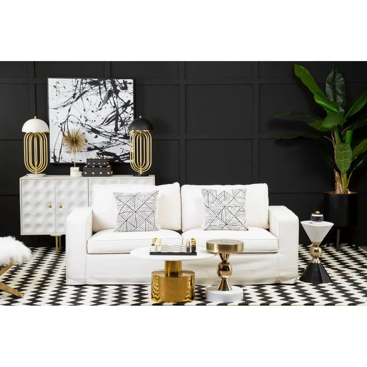 Modern living room with white sofa, geometric cushions, gold accent tables, black wall