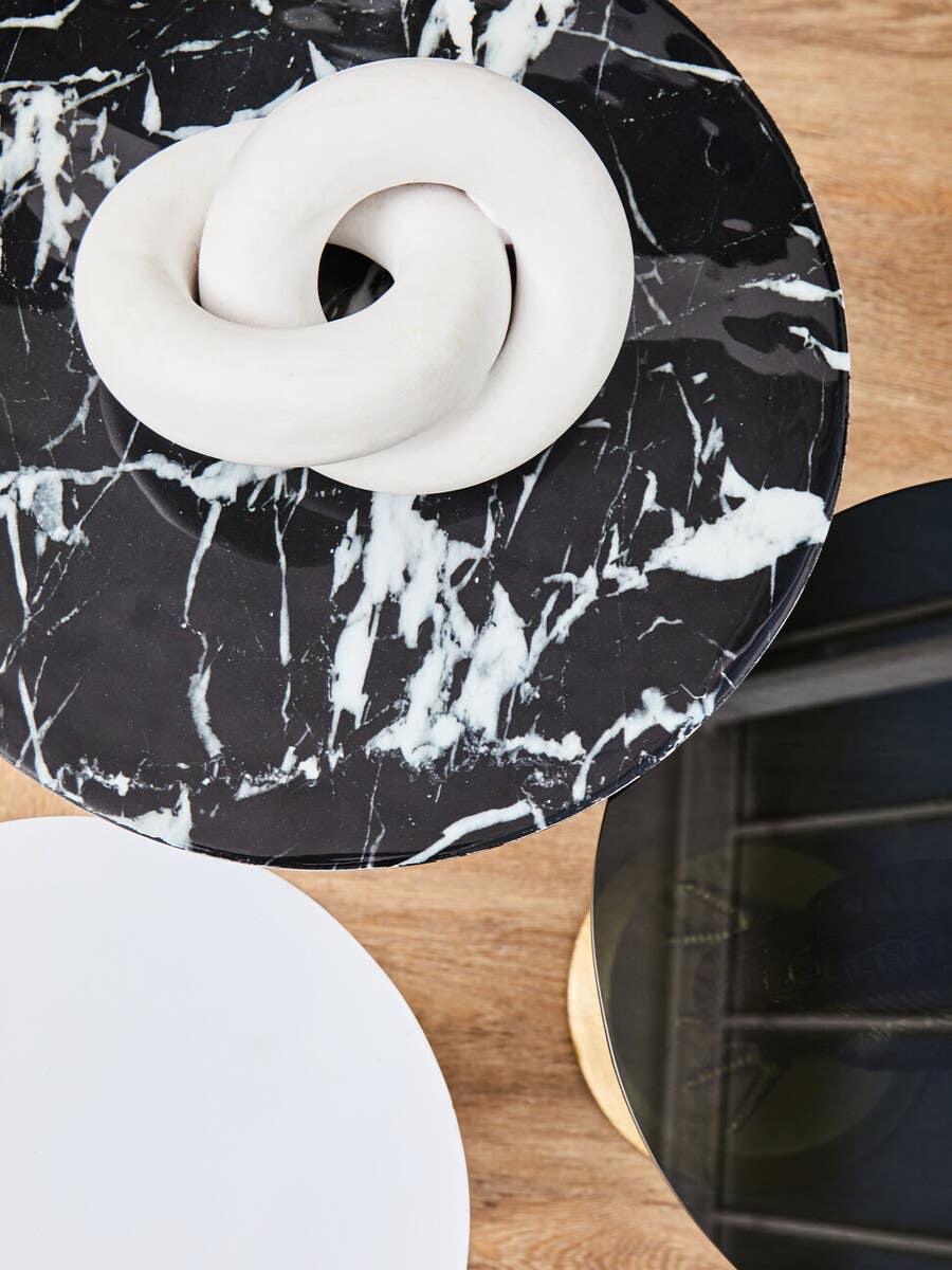 Black marble side table with sculptural white knot decor on wooden floor